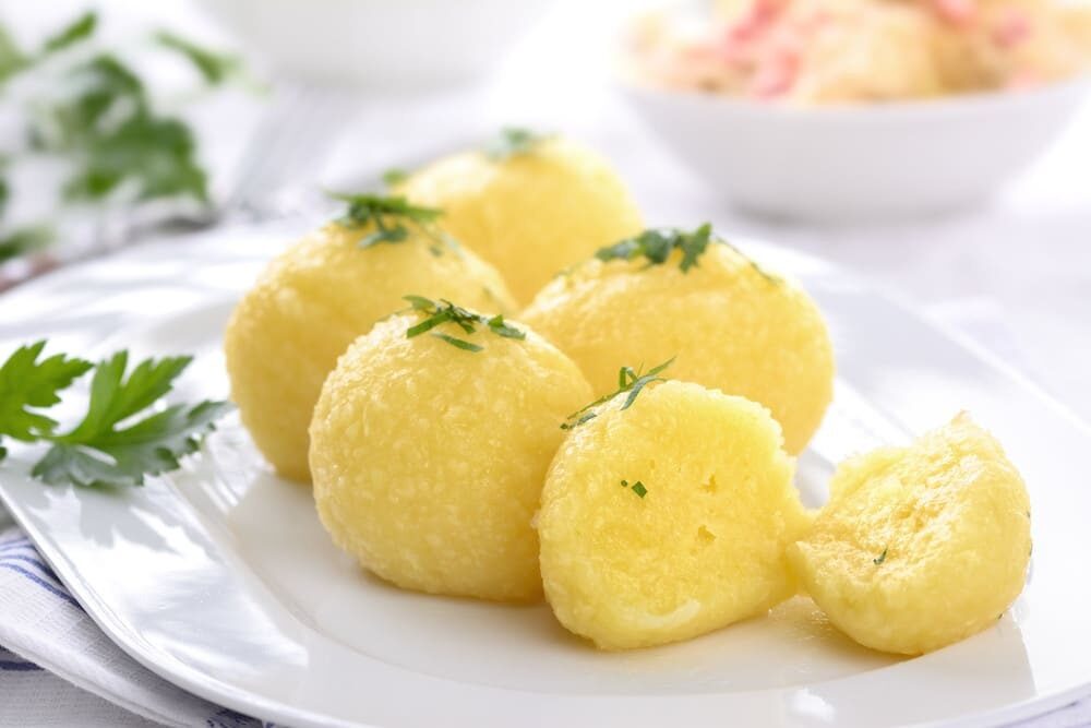 Светлые картофельные клёцки со сливочным маслом и зеленью на белой тарелке