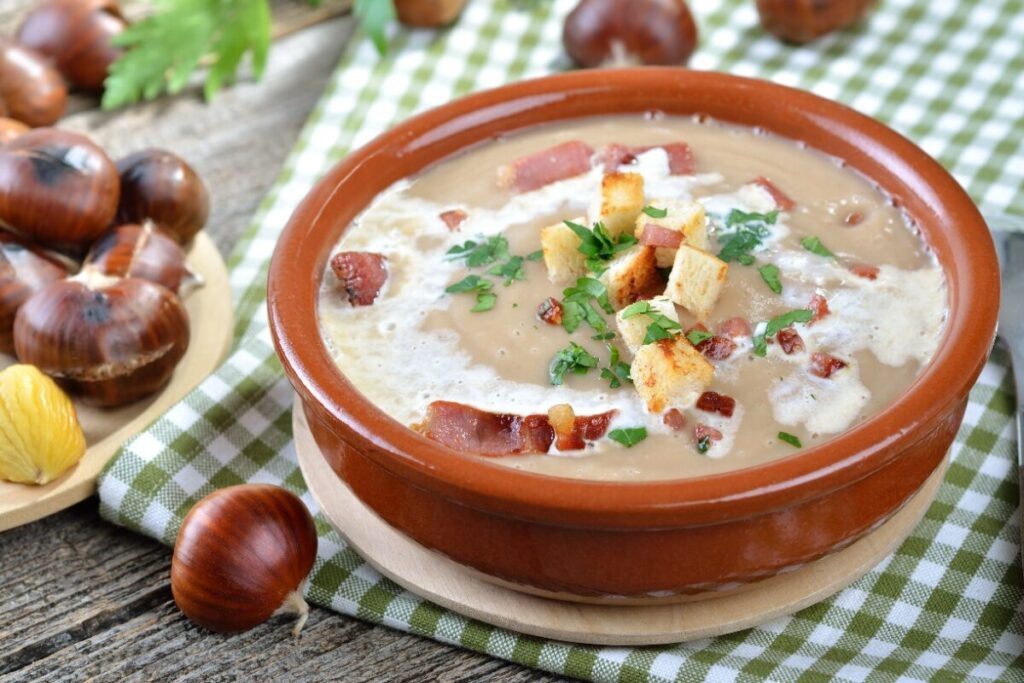 Каштановый крем-суп с беконом и сухариками в глиняной миске.
