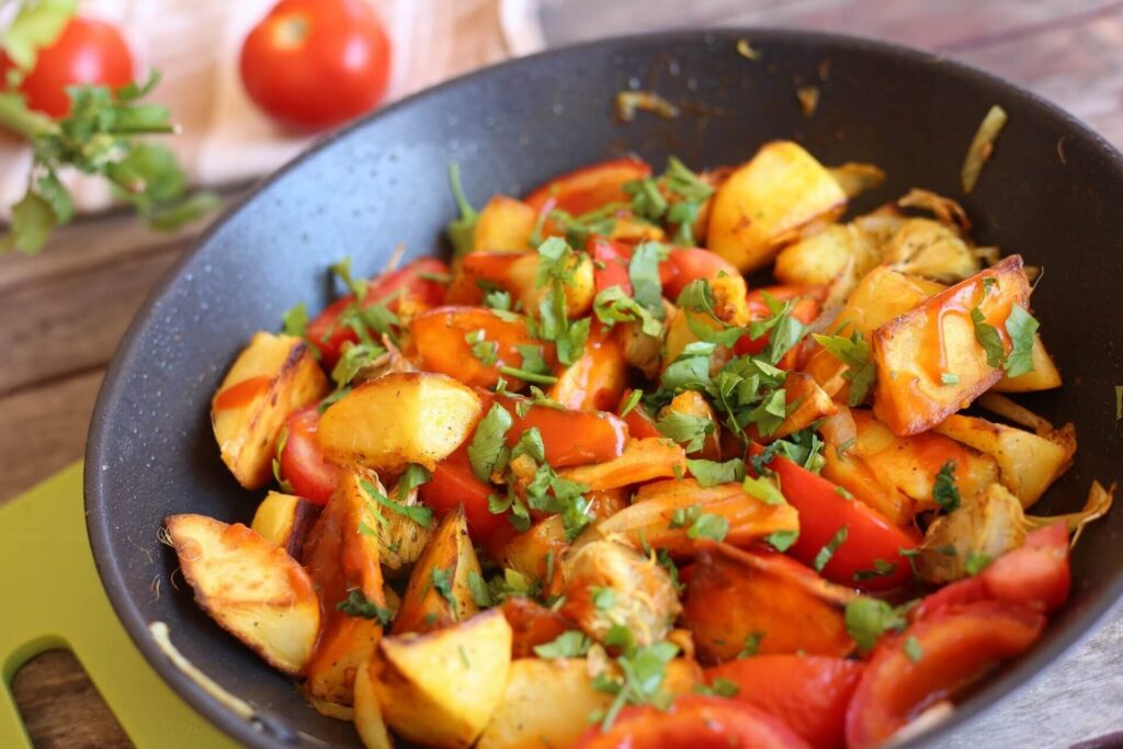 Картофель с артишоками и красными помидорами на чёрной сковороде