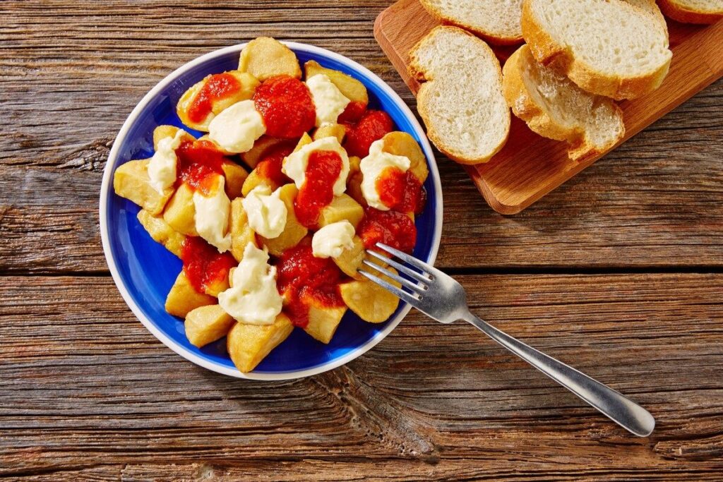 Румяные картофельные кубики с красным и белым соусами в синей тарелке