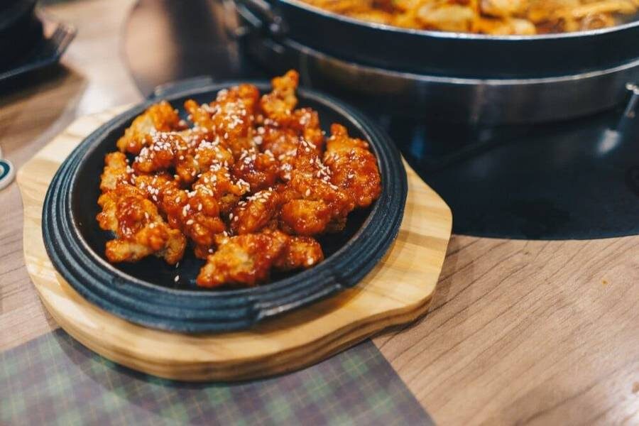 Глазированные куриные кусочки с кунжутом лежат на чёрной тарелке.