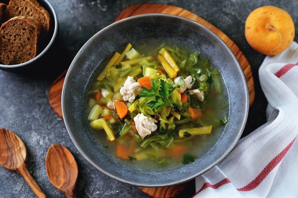 Куриный суп с капустой и овощами в тёмной тарелке