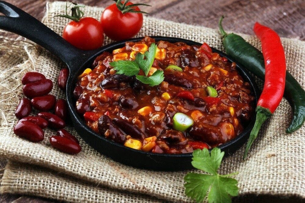 Густое чили с красной фасолью, фаршем и кукурузой в чёрной сковороде