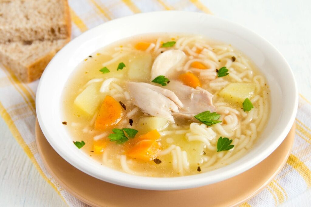 Куриный суп с картофелем, морковью, лапшой и петрушкой в белой тарелке