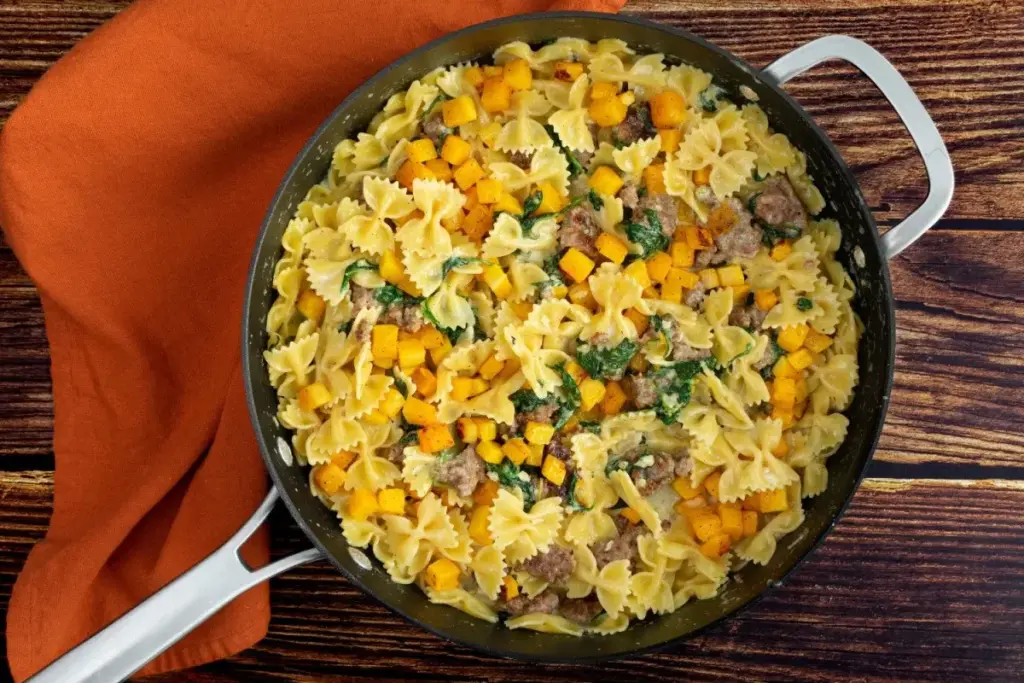 Макароны с жёлтыми тыквенными кубиками, фаршем и зелёным шпинатом в сковороде