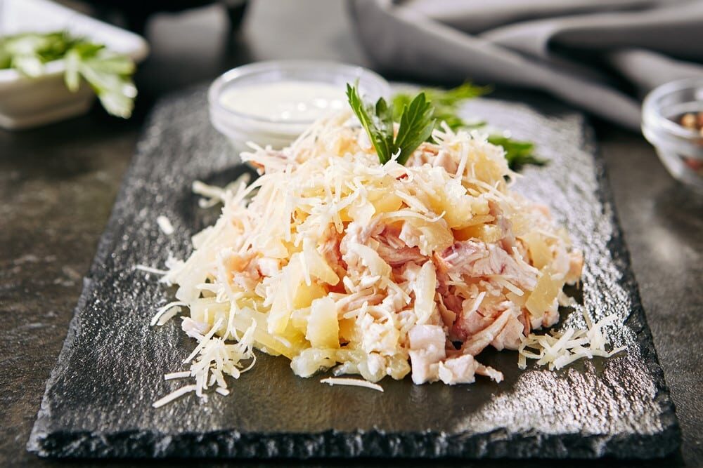 Салат с курицей и ананасом под мелко натёртым белым сыром на прямоугольной тарелке