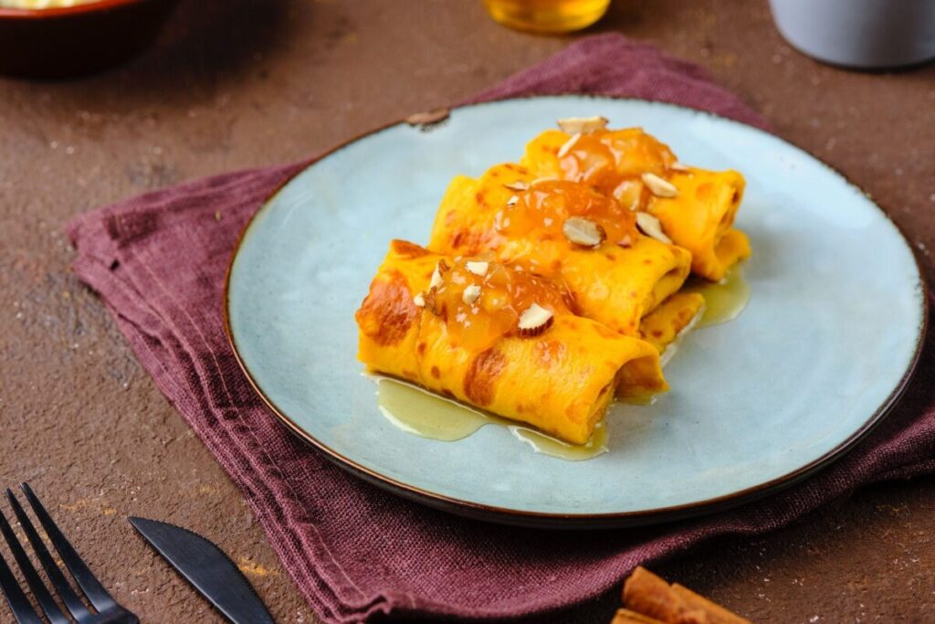 Сложенные тыквенные блины с оранжевыми кусочками тыквы на голубой тарелке