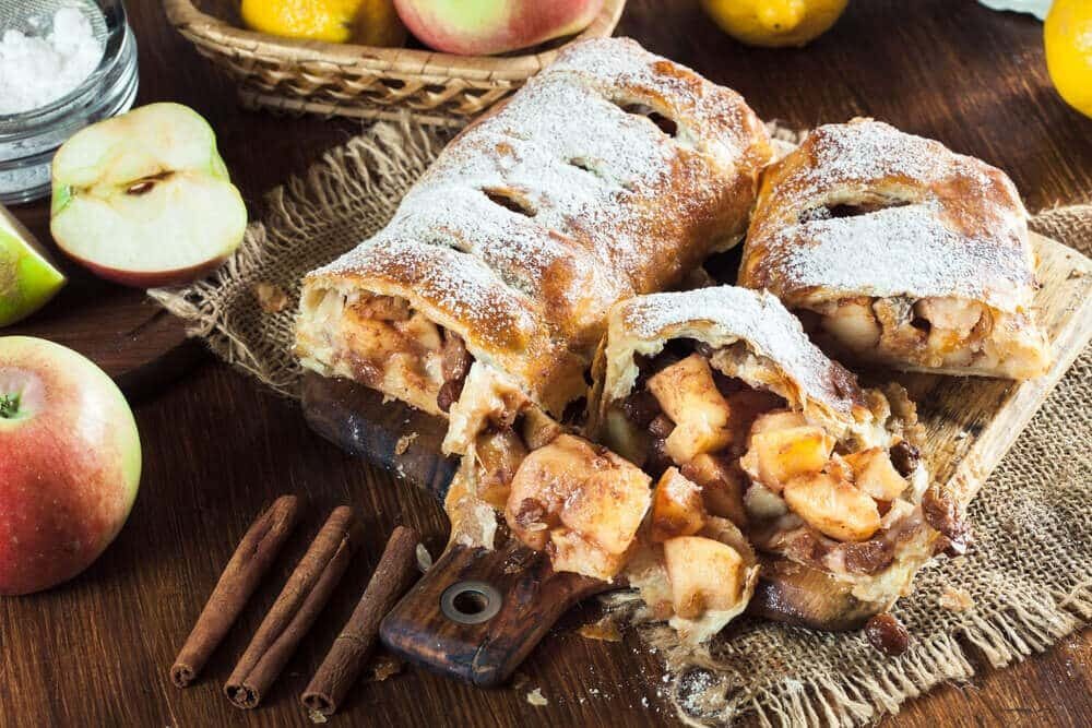 Нарезанный яблочный штрудель с изюмом и сахарной пудрой на тарелке
