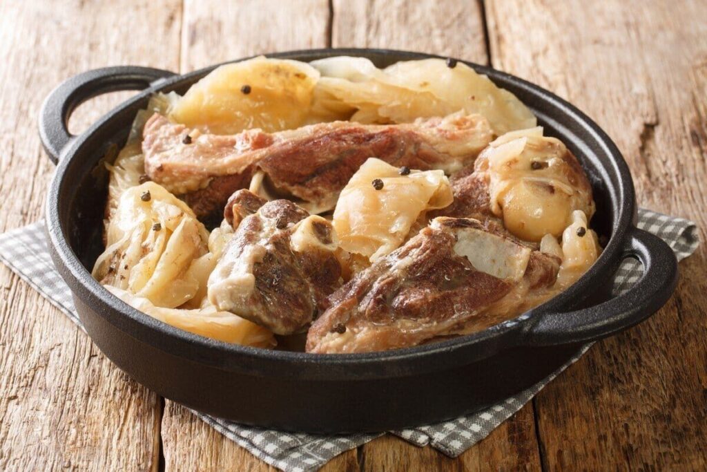 Куски тушёной баранины с крупными дольками капусты в чёрной кастрюле