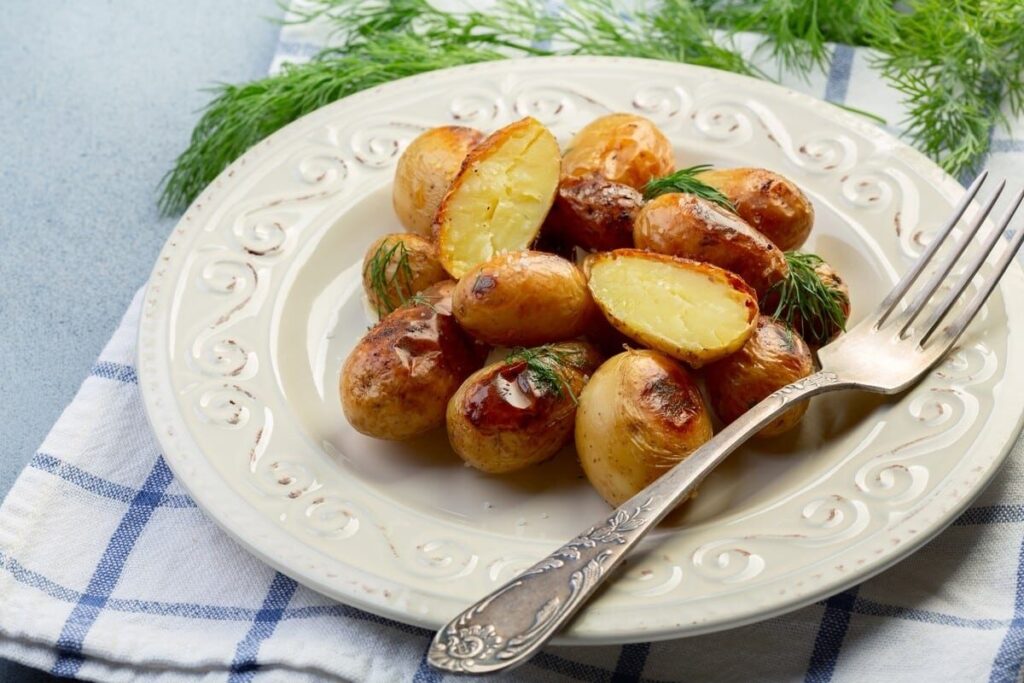 Запечённые половинки молодого картофеля с кожурой и зеленью на белой тарелке