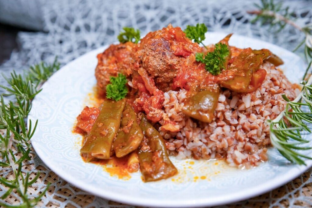 Гречка с фрикадельками, стручковой фасолью и красным томатным соусом на тарелке