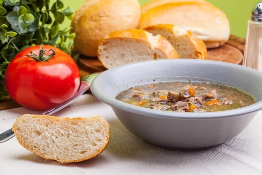 Куриный суп с желудочками и овощами в серой миске, рядом хлеб