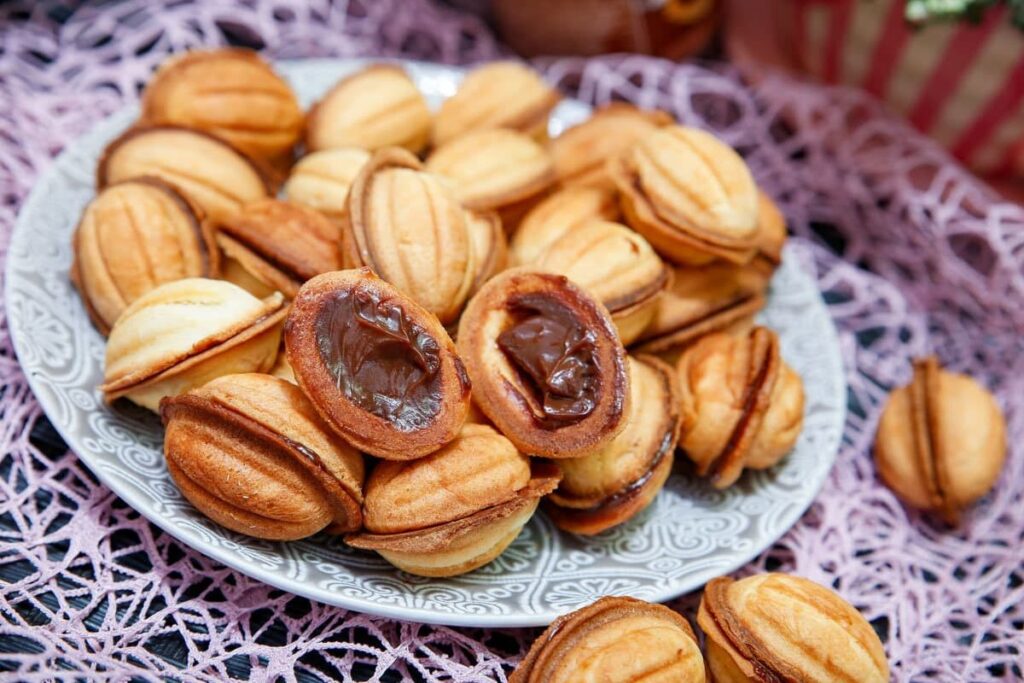 Печенье орешки со светлыми скорлупками и шоколадной начинкой на тарелке