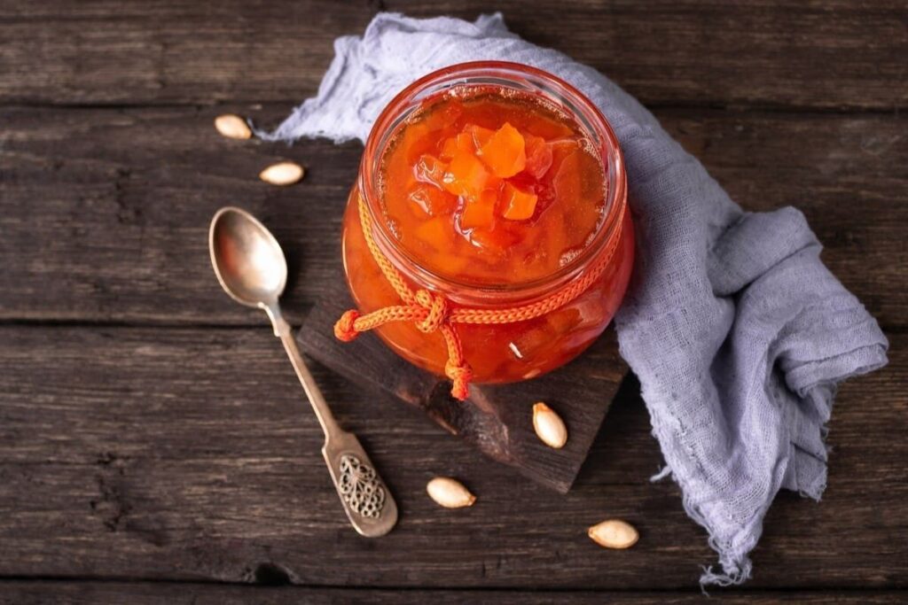 Кусочки оранжевой тыквы в сиропе в стеклянной банке рядом с пряностями