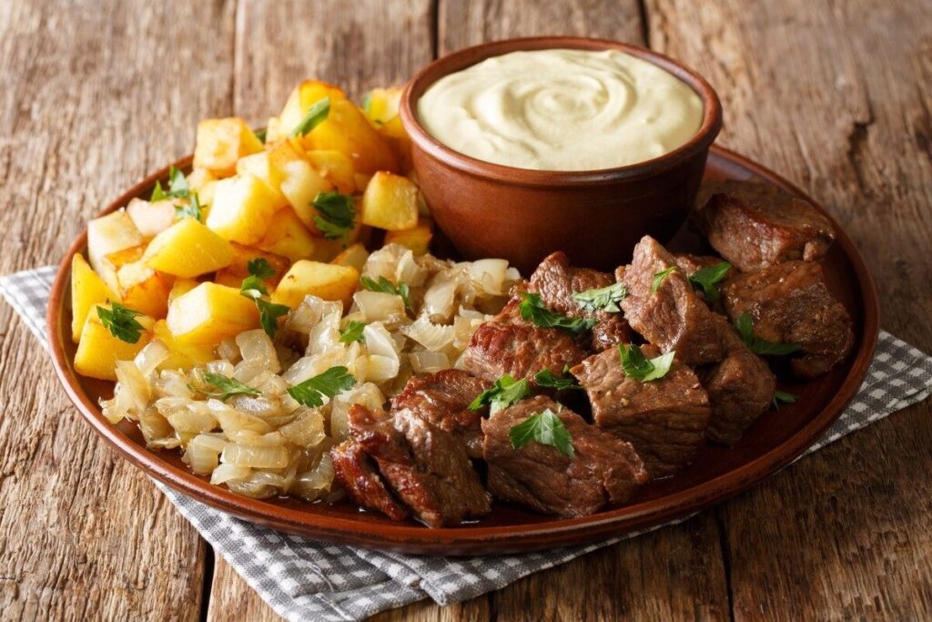 Кусочки говядины, жареный картофель и лук на овальной тарелке