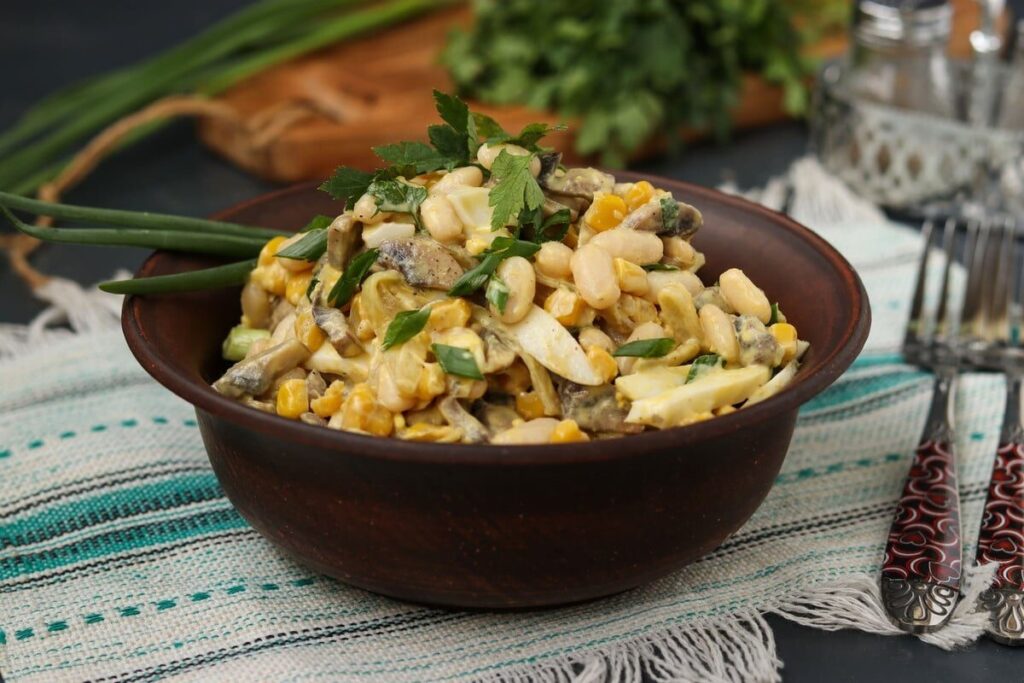 Салат с белой фасолью, кукурузой, яйцами и грибами в тёмной миске