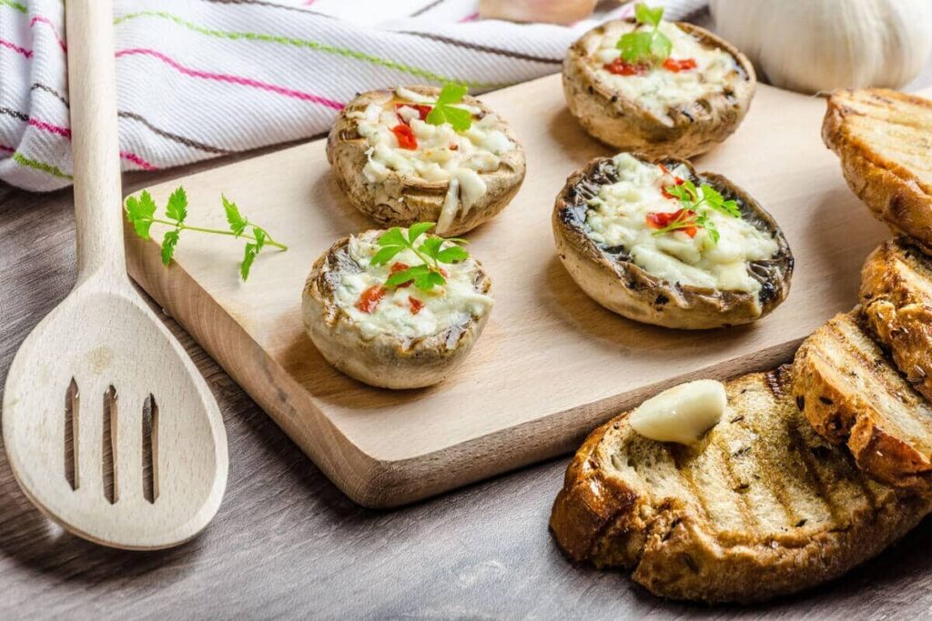 Фаршированные шампиньоны с расплавленным сыром и зеленью на доске