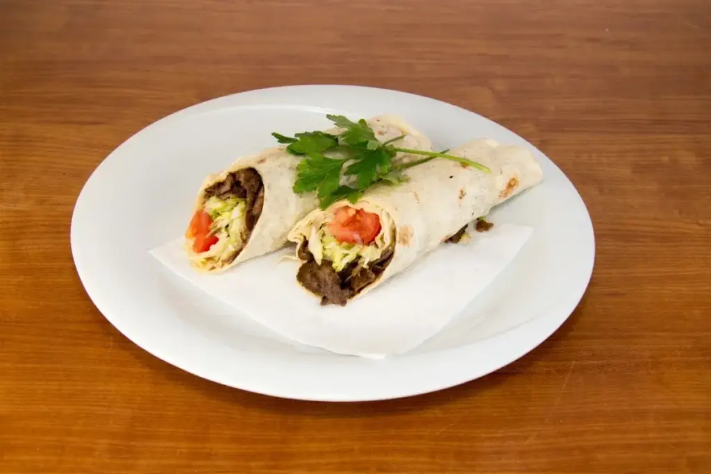 Два разрезанных рулета в тонком лаваше с мясом и овощами на белой тарелке