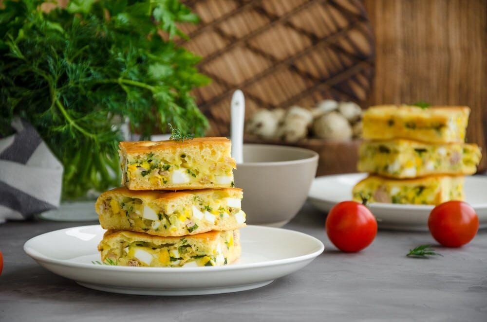 Кусочки заливного пирога с яйцами и зелёным луком на белой тарелке